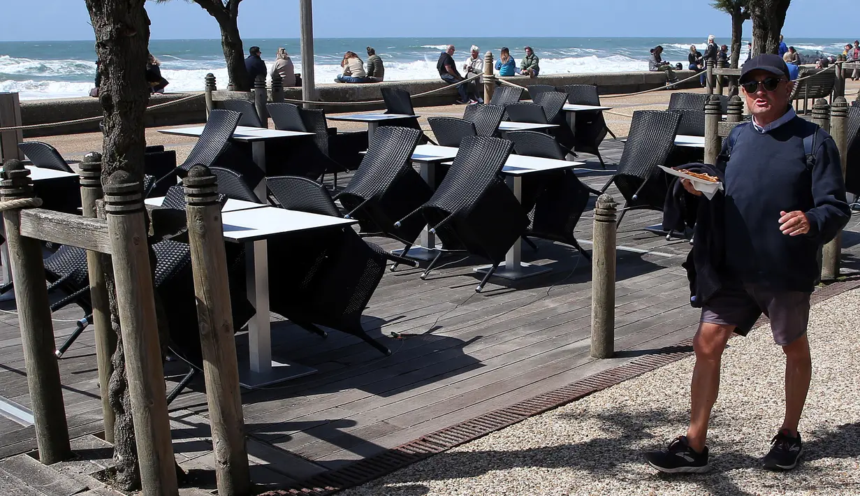 Seorang pria berjalan di dekat teras restoran yang siap buka kembali di Anglet, barat daya Prancis, Senin (17/5/2021). Restoran, kafe, dan bioskop sebagian akan dibuka kembali pada hari Rabu, 19 Mei mendatang. (AP Photo/Bob Edme)