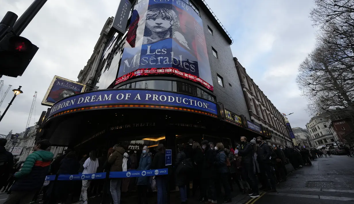 Orang-orang mengantre mengenakan masker melawan virus corona, di luar teater untuk pertunjukan Les Miserables di London, Selasa (28/12/2021). Inggris kini dilanda lonjakan kasus harian terlebih setelah muncul varian Omicron. (AP Photo/Alastair Grant)