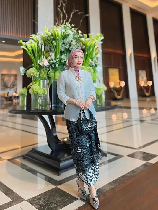 Imel PC hadir di acara pernikahan anak Elma dengan mengenakan kebaya kartini warna putih yang dipadukan hijab segi empat berwarna pink, serta dipermanis dengan bros emasnya. [@imelpc].