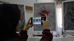 Seorang perempuan memotret karya seni di pameran seniman Palestina Kholoud al-Dasooqi di Gaza City, 11 Agustus 2020. Seniman asal Kota Khan Younis di Jalur Gaza itu menggelar pameran selama dua hari untuk mengungkap kekerasan terhadap perempuan melalui puluhan lukisan. (Xinhua/Rizek Abdeljawad)