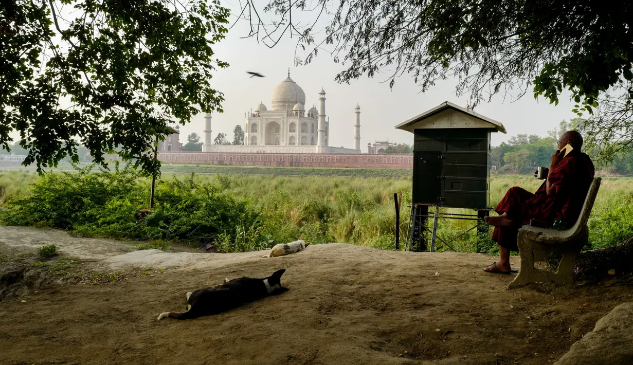 Biksu Buddha duduk di seberang Taj Mahal dari tepi sungai Yamuna di Agra, Jumat (4/5). Sejumlah pihak mengatakan perubahan warna Taj Mahal kemungkinan besar disebabkan pembangunan konstruksi di sekitarnya dan kotoran serangga. (AFP/CHANDAN KHANNA)