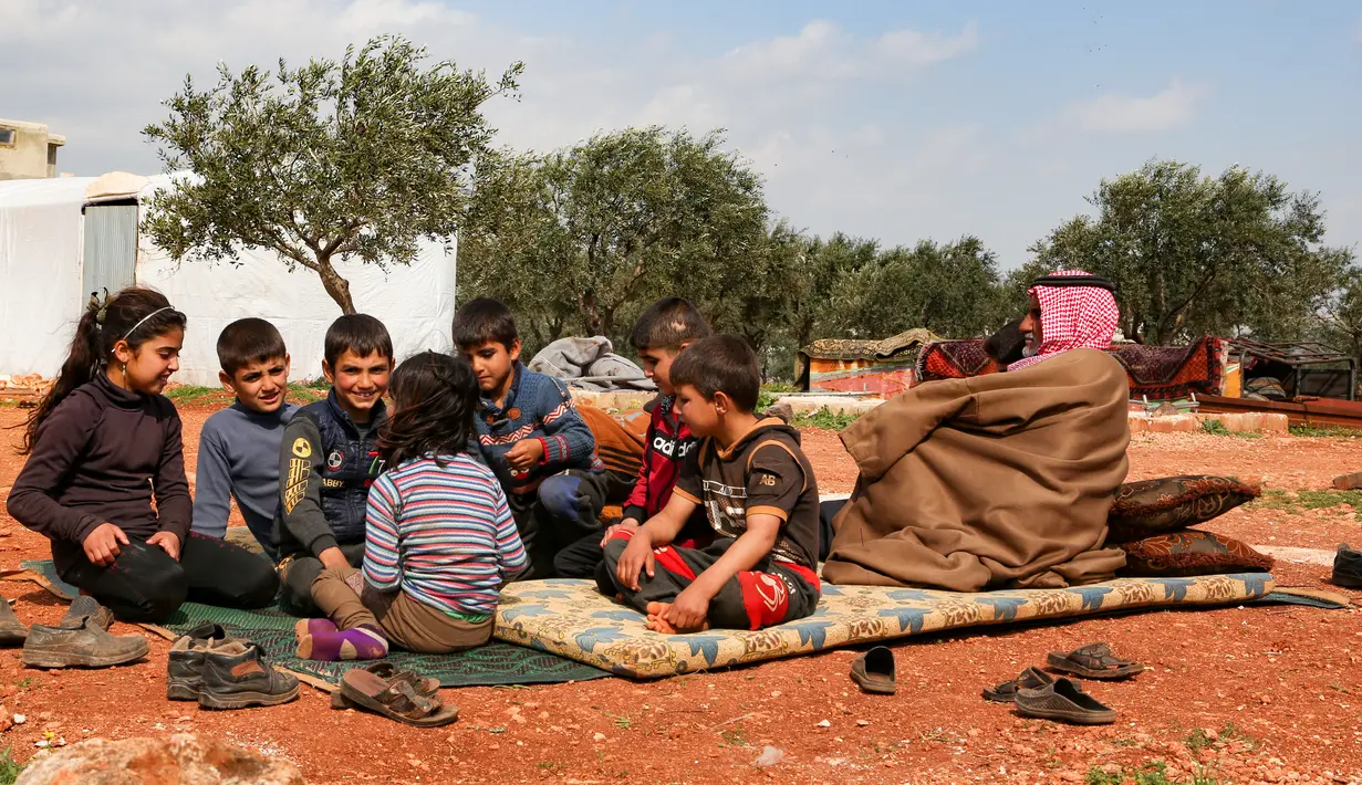 Abderrazaq Khatoun, beristirahat dengan 11 cucunya yang yatim piatu di luar tenda di desa Harbanoush, di Idlib, Suriah pada 11 Maret 2021. Perang Suriah yang merampas 13 anak Khatoun dan salah satu istrinya, membuat kakek 83 tahun itu membesarkan 11 cucu yatim piatu sendirian. (Ahmad al-ATRASH/AFP)