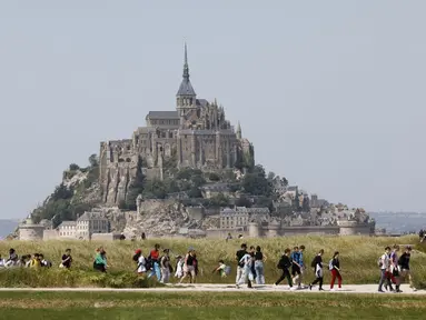 Orang-orang berjalan melewati Biara Mont-Saint-Michel saat kunjungan Presiden Prancis Emmanuel Macron di Normandia, Le Mont-Saint-Michel, Prancis, Senin (5/6/2023). (Ludovic MARIN/POOL/ AFP)