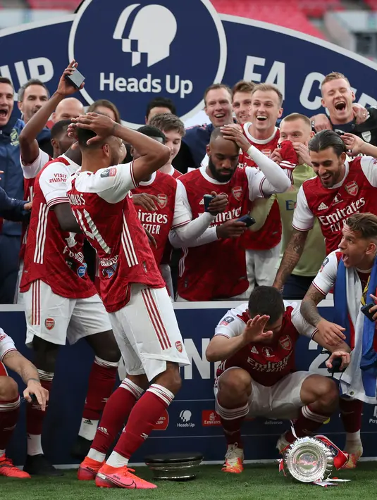 Striker Arsenal, Pierre-Emerick Aubameyang (tengah) menjatuhkan trofi saat merayakan gelar juara Piala FA usai mengalahkan Chelsea pada pertandingan final Piala FA di stadion Wembley, Minggu (2/8/2020).  Aubameyang terlihat kaget sambil memegang kepalanya saat trofi terjatuh. (Adam Davy/Pool via AP)
