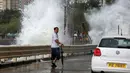 Seorang warga melintas di dekat ombak besar di pesisir Hong Kong, Tiongkok, Jumat (21/10). Banyak warga mengabaikan peringatan dan menyaksikan hantaman ombak besar yang menghantam pesisir tersebut. (REUTERS/Bobby Yip)