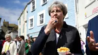 Perdana Menteri (PM) Inggris, Theresa May mencicipi beberapa keripik saat berhenti untuk kampanye di Mevagissey, Cornwall, Selasa (2/5). Theresa May melakukan kampanye dengan berkeliling jalanan di Cornwall. (Dylan Martinez/PA via AP)