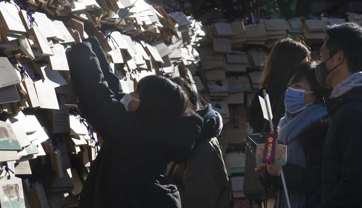 Orang tua melihat putri mereka menggantung papan "ema" dengan keinginan mereka tertulis di atasnya di kuil Yushima Tenmangu di Tokyo pada Hari Tahun Baru, Jumat (1/1 Januari 2021. (AP Photo/Hiro Komae)
