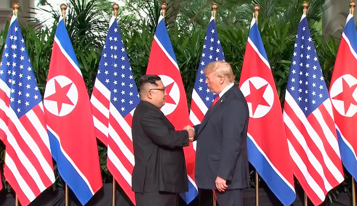 Presiden AS Donald Trump  berjabat tangan dengan Pemimpin Korea Utara, Kim Jong-un dalam pertemuan bersejarah di resor Capella, Pulau Sentosa, Selasa (12/6). Trump dan Kim berjabat tangan untuk pertama kalinya. (Host Broadcaster Mediacorp Pte Ltd via AP)