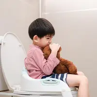 Potret seorang anak sedang berlatih menggunakan toilet dengan bangku tambahan dan ditemani dengan boneka beruang kesayangannya. (Foto dok: Freepik/dumsdumdum).