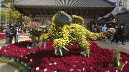Orang-orang memakai masker berjalan di dekat dinosaurus yang terbuat dari bunga krisan selama festival Krisan di kuil Chogyesa, Seoul, Senin (19/10/2020). Korsel mulai menguji puluhan ribu karyawan rumah sakit dan panti jompo untuk mencegah wabah COVID-19. (AP Photo/Ahn Young-joon)