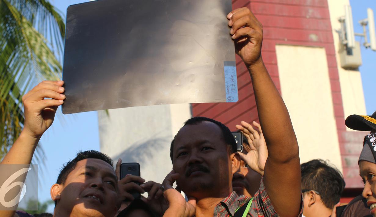 Warga mengunakan film bekas ronsen melihat proses Gerhana Matahari Total (GMT) 2016 di halaman Taman Ismail Marzuki (TIM), Jakarta, Rabu (9/3). Fenomena alam ini terjadi setiap 350 tahun. (Liputan6.com/Fery Pradolo)