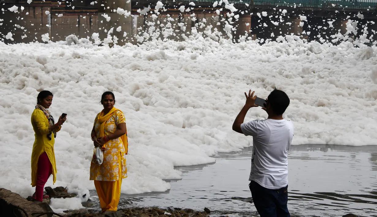 Pengunjung berfoto dengan latar belakang busa yang memenuhi sungai Yamuna di kota New Delhi, India, 23 September 2018. Akibat pertumbuhan populasi dan industrialisasi, Sungai Yamuna menjadi salah satu sungai paling tercemar di dunia. (AFP/Dominique FAGET)