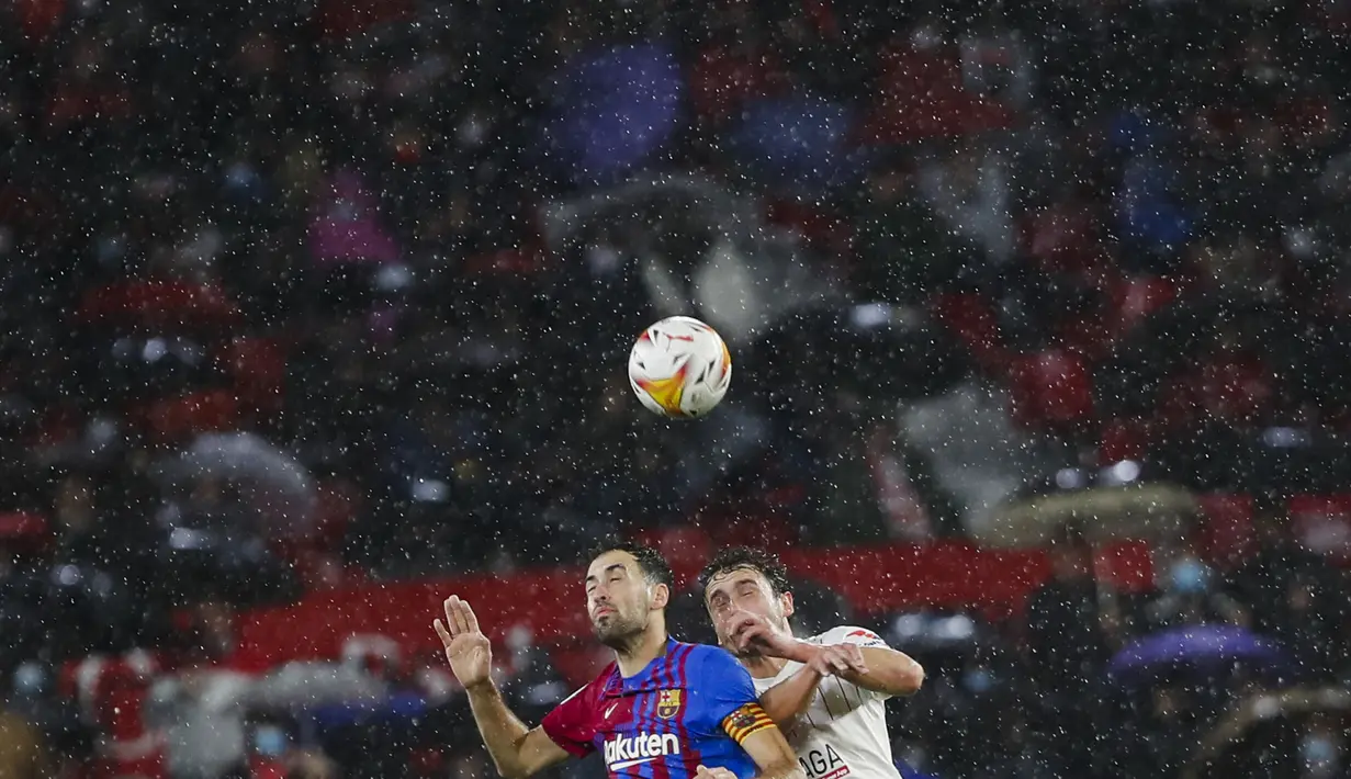Gelandang Barcelona, Sergio Busquets berebut bola udara dengan pemain Sevilla, Thomas Delaney pada pertandingan La Liga Spanyol di stadion Ramon Sanchez-Pizjuan, Spanyol, Rabu (22/12/2021). Hasil ini tidak mengubah posisi Barcelona pada peringkat ketujuh dengan 28 poin. (AP Photo/Angel Fernandez)