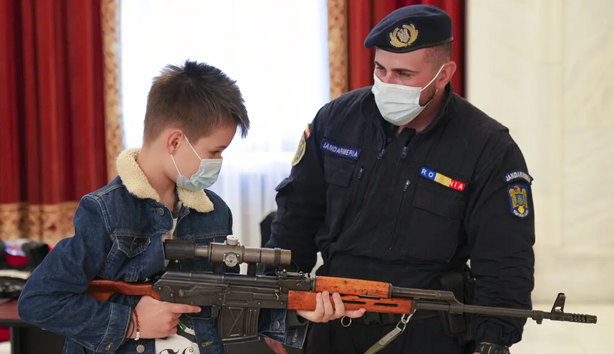 Seorang anak laki-laki memegang senjata di stand yang didirikan oleh gendarmerie Rumania di Istana Parlemen pada Hari Anak Internasional di Bukares, Rumania, Selasa (1/6/2021). Orang-orang memanfaatkan kesempatan untuk mengunjunginya secara gratis. (AP Photo/Vadim Ghirda)