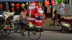 Seorang pedagang mengendarai sepeda melewati balon Santa Claus dan barang-barang hiasan Natal lainnya yang dipajang untuk dijual di sebuah toko di pinggir jalan di Thiruvananthapuram, negara bagian Kerala, India, (17/12). (AP Photo / R S Iyer)