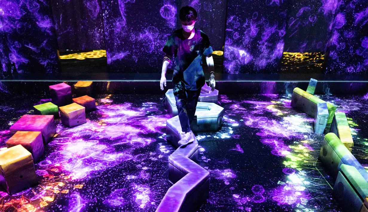 Seorang anggota staf berjalan melalui instalasi digital interaktif "Balance Stepping Stones through the Invisible World" selama pratinjau media "teamLab Forest" di gedung hiburan BOSS E・ZO FUKUOKA di Fukuoka, Jepang, Jumat (16/7/2021). (YUKI IWAMURA/AFP)