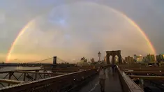 Pejalan kaki melintasi Jembatan Brooklyn saat pelangi menghiasi langit New York City, AS (15/5). Jembatan Brooklyn adalah salah satu jembatan suspensi tertua di Amerika Serikat. (AFP Photo/Hector Retamal)