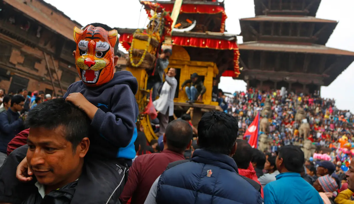 Seorang anak mengenakan topeng duduk di pundak ayahnya saat mengikuti festival Bisket Jatra di Bhaktapur, Nepal (10/4). Festival ini diadakan untuk menandai Tahun Baru Nepal.  (AP Photo/Niranjan Shrestha)