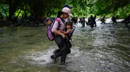 Seorang migran Haiti membawa seorang anak melintasi Celah Darien dari Kolombia ke Panama Sabtu, (15/10/2022). Perjalanan Kelompok Imigran tersebut berharap mencapai Amerika Srikat (AS).(Fernando Vergara/AP)