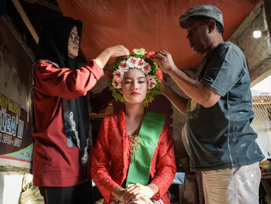 Seorang perempuan dengan pakaian tradisional dibantu menyiapkan hiasan bunga di rambutnya untuk berpartisipasi dalam Festival Ngarot di Lelea, Indramayu , Jawa Barat, pada 13 Desember 2023. (Timur MATAHARI/AFP)