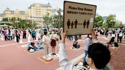 Pengunjung mengenakan masker saat menjaga jarak untuk antre memasuki Tokyo Disneyland di Urayasu, dekat Tokyo, Rabu (1/7/2020). Tokyo Disneyland dibuka kembali untuk pertama kalinya dalam empat bulan setelah sempat ditutup karena penyebaran Covid-19. (Kyodo News via AP)