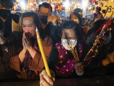 Warga yang mengenakan masker membakar dupa pertama mereka saat berdoa di Kuil Wong Tai Sin untuk merayakan Tahun Baru Imlek yang menandai Tahun Kelinci, di Hong Kong, Sabtu, 21 Januari 2023. Asap dupa memenuhi udara satu jam menjelang Tahun Baru Imlek di Kuil Wong Tai Sin Hong Kong. (AP Photo/Bertha Wang)