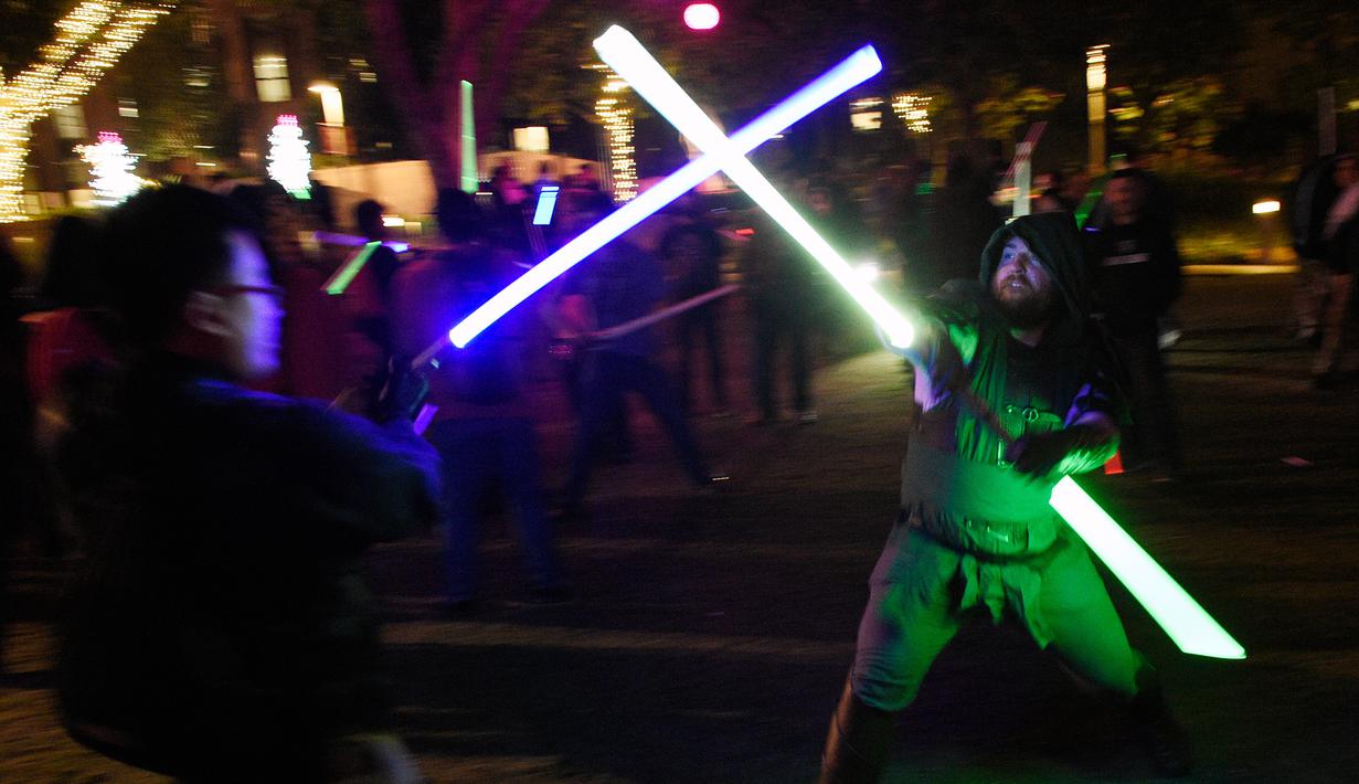Dua orang pria saling beradu lightsaber (pedang sinar) saat mengikuti Glow Battle Tour di Grand Park, Los Angeles (15/12). Para penggemar ini berkumpul dengan membawa pedang sinar yang beraneka warna. (Photo by Chris Pizzello/Invision/AP)
