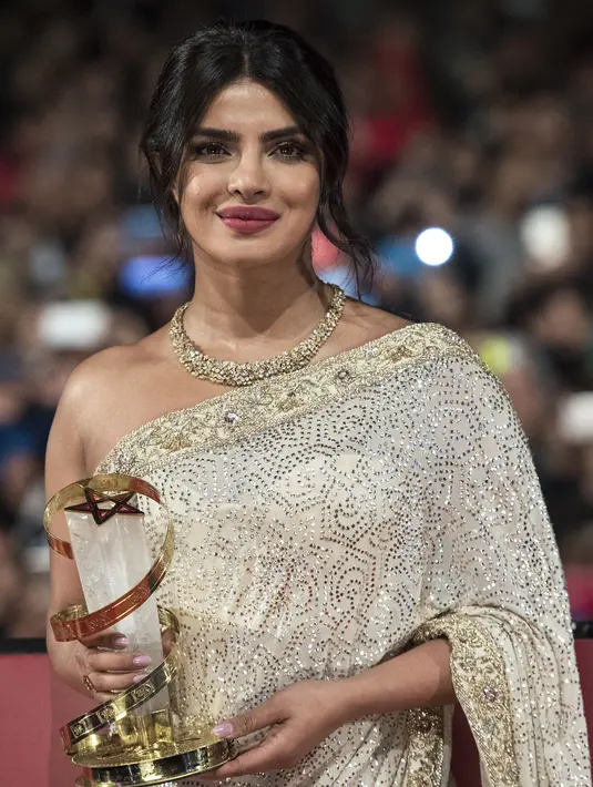 Aktris Priyanka Chopra berpose dengan piala penghargaan saat menghadiri Festival Film Internasional Marrakech ke-18 di Jemaa El Fnaa, Marrakech (5/12/2019). Priyanka Chopra tampil cantik memesona mengenakan busana sari emas dan brokat perak denga dengan kalung emas di lehernya. (AFP/Fadel Senna)