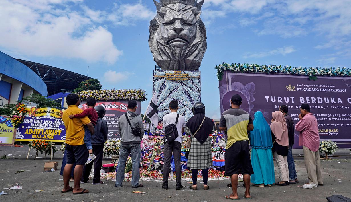 Orang-orang berdoa dekat patung singa, maskot Arema FC, di luar Stadion Kanjuruhan, Malang, Jawa Timur, Selasa (4/10/2022). Polri menjatuhkan sanksi kepada 10 anggota polisi dan menyelidiki 18 orang lainnya buntut tragedi kerusuhan yang menewaskan 125 orang di Stadion Kanjuruhan. (AP Photo/Dicky Bisinglasi)
