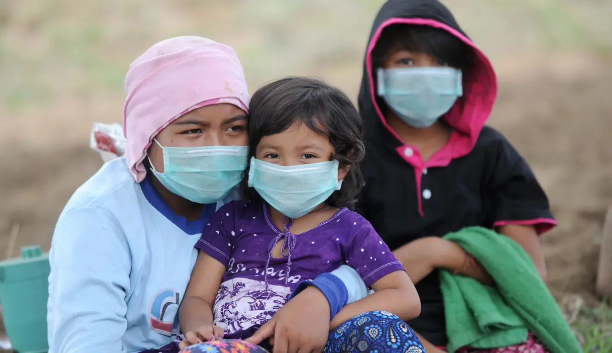 Sebuah keluarga mengenakan masker saat beraktivitas di kecamatan Kubu, Kabupaten Karangasem, Bali (27/11). Pejabat setempat juga mengimbau agar warga menggunakan masker untuk mengantisipasi adanya debu vulkanik. (AFP/Sonny Tumbelaka)