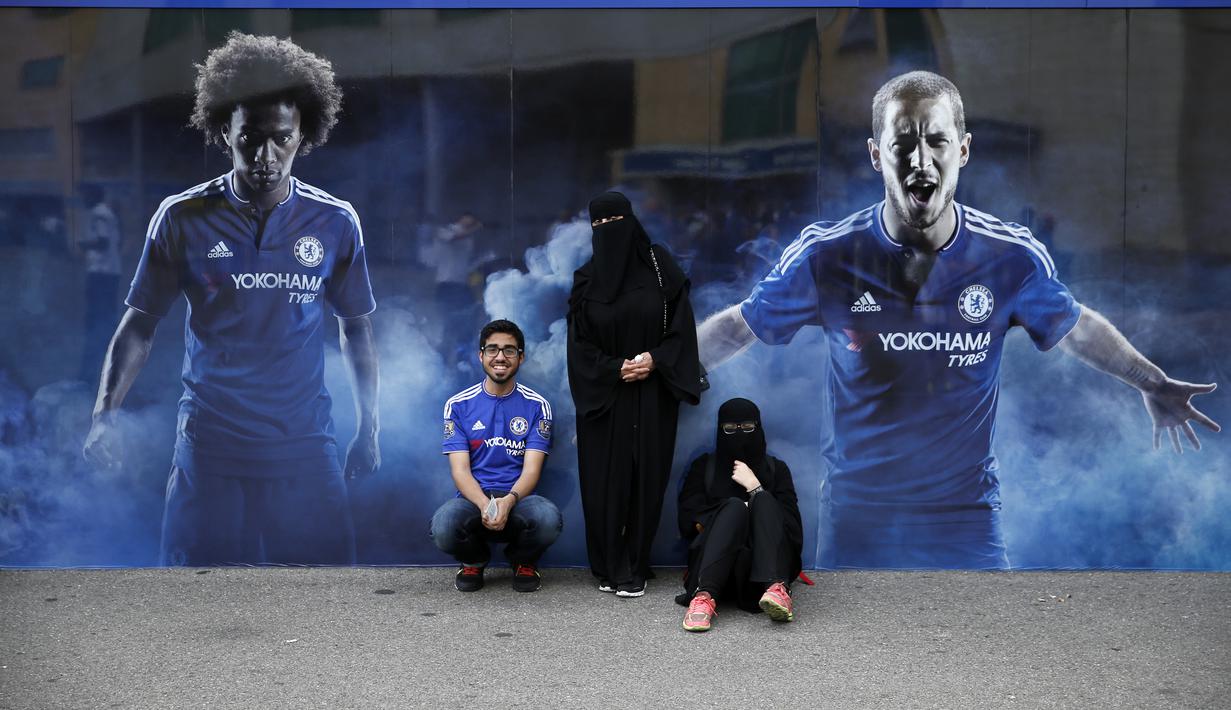 Suporter Chelsea berfoto dengan latar poster pemain Chelsea di luat stadion Stamford Bridge. (AFP Photo/Adrian Dennis)