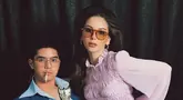 Dalam foto ini, Al Ghazali duduk di kursi dengan mengenakan setelan jas biru tua yang khas, lengkap dengan kemeja berkerah lebar yang terbuka. Dengan tatapan tajam, ia memegang tongkat yang mirip dengan gaya Elvis Presley, menambah kesan berani dan karismatik. Di sampingnya, Alyssa Daguise tampil anggun dalam balutan atasan ungu muda yang bertekstur, mengingatkan kita pada gaya Priscilla yang ikonik. (Liputan6.com/IG/@alyssadaguise)