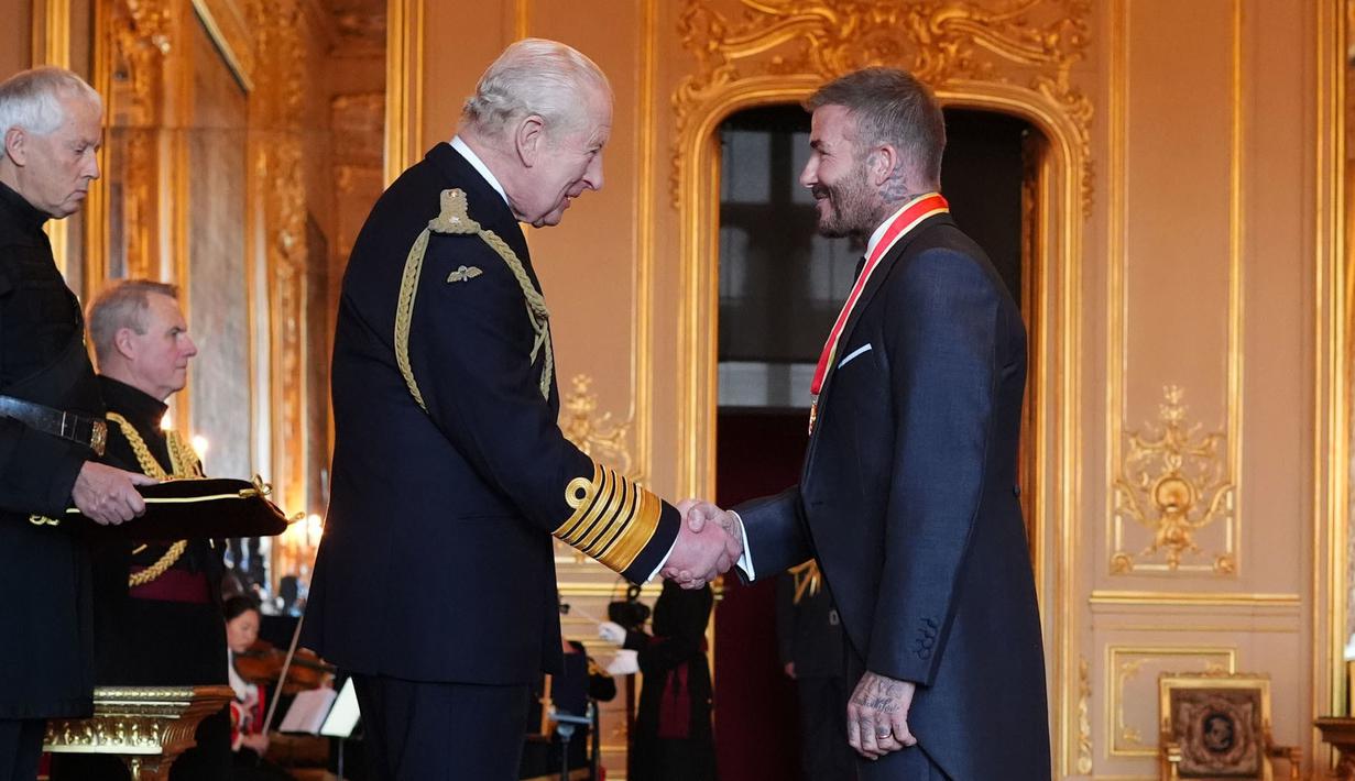Mantan pesepak bola, David Beckham (kanan) berjabat tangan dengan Raja Inggris, Charles III setelah upacara penobatan gelar Ksatria di Kastil Windsor, Berkshire, Inggris, Selasa (04/11/2025) waktu setempat. (AP Photo/PA/Jonathan Brady)