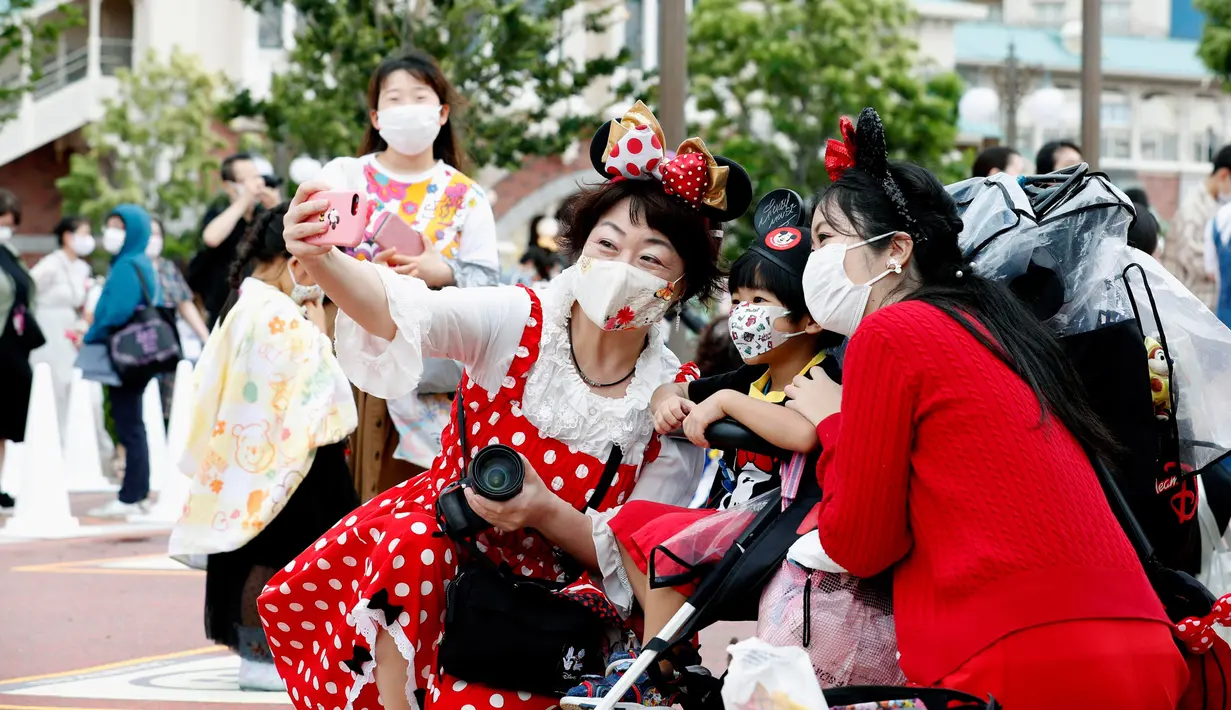 Pengunjung mengenakan masker guna melindungi diri dari virus corona berswafoto sebelum memasuki Tokyo Disneyland di Urayasu, dekat Tokyo, Rabu (1/7/2020). Tokyo Disneyland dibuka kembali untuk pertama kalinya dalam empat bulan setelah sempat ditutup karena penyebaran Covid-19. (AP/ Koji Sasahara)