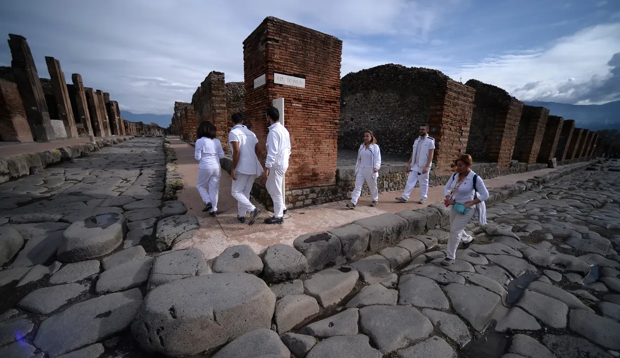 Wisatawan berjalan melewati Via del Vesuvio (kiri) yang berbatu, Pompeii, Italia, Senin (25/11/2019). Meski butuh 1.500 tahun untuk ditemukan, kondisi rumah, benda-benda, hingga jenazah warga Pompeii masih cukup utuh saat ditemukan. (Filippo MONTEFORTE/AFP)