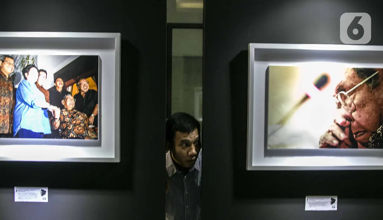 Pengunjung mengintip dari celah-celah pada pameran Satu Dekade Haul Presiden ke IV Republik Indonesia KH Abdurrahman Wahid atau Gus Dur di Kantor DPP PKB, Jakarta, Rabu (15/1/2020). Pameran sekaligus lomba foto ini diikuti oleh puluhan fotografer dari seluruh Indonesia. (Liputan6.com/Faizal Fanani)