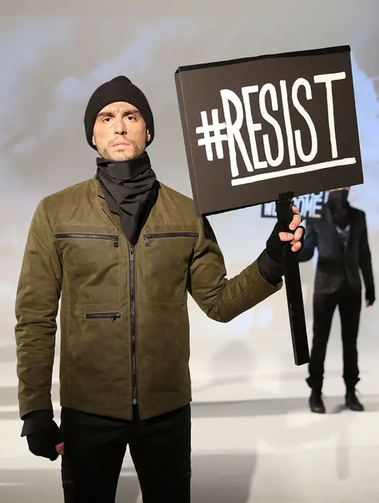 Model berpose dengan poster #Resist saat presentasi karya desainer Robert James dalam New York Fashion Week (NYFW) di New York,AS  (30/1). Presentasi ini menampilkan poster-poster yang menyindir kebijakan Donald Trump. (Robin Marchant Getty Images/AFP)