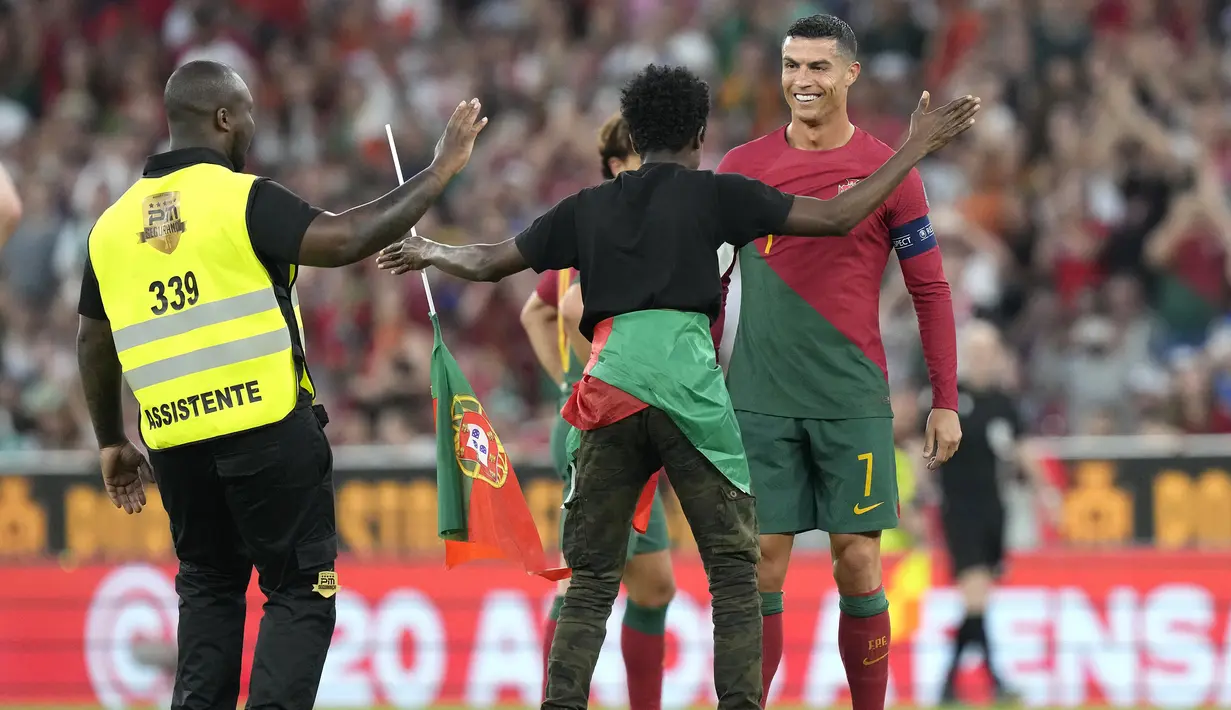 Striker Timnas Portugal, Cristiano Ronaldo tersenyum saat seorang penyusup lapangan menghampirinya di tengah laga Grup J Kualifikasi Euro 2024 antara Timnas Portugal menghadapi Bosnia Herzegovina di Luz Stadum, Lisbon, Portugal, Minggu (18/6/2023) dini hari WIB. (AP Photo/Armando Franca)