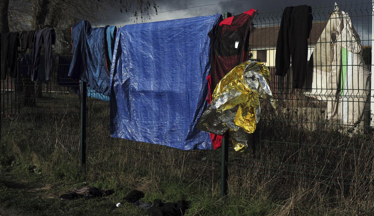 Barang-barang migran digantung di pagar di kamp darurat di luar Calais, Prancis utara, Sabtu (277/11/2021). Di kamp-kamp darurat di luar Calais, para migran yang putus asa menunggu kesempatan untuk mencoba menyeberangi Selat Inggris. (AP Photo/Rafael Yaghobzadeh)