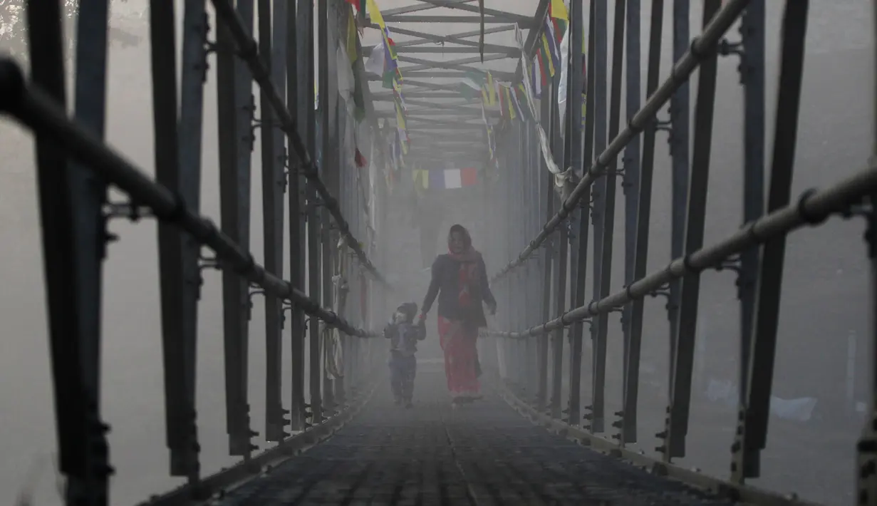 Seorang wanita Nepal menyusuri jembatan bersama anaknya untuk mengikuti festival Gaya Aunsi di Kathmandu, Nepal (21/12). Ritual suci ini digelar untuk memberi doa dan penghormatan kepada anggota keluarga yang telah meninggal. (AP Photo/Niranjan Shrestha)