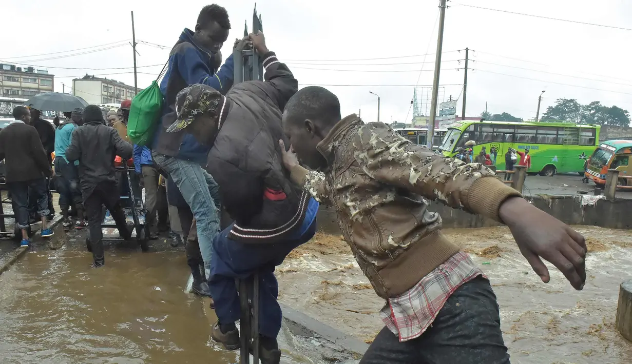 Pejalan kaki berjalan di pagar untuk menyebrang menyusuri jalan yang banjir menuju tempat kerja setelah hujan deras di Nairobi, Kenya (15/3). (AFP Photo/Simon Maina)