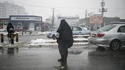 Seorang wanita mengenakan burqa memohon di sepanjang jalan saat hujan salju di Kabul (4/1/2022). Sedikitnya tujuh warga Afghanistan tewas dan 26 lainnya cedera dalam beberapa kecelakaan lalu lintas. (AFP/Mohd Rasfan)