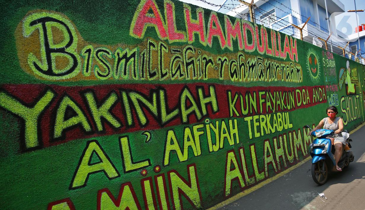 Pengendara melintasi mural bernuansa Islami di Gang Pelangi, kawasan Kalibata, Jakarta, Jumat (23/4/2021). Mural bernuansa Islami tersebut dibuat untuk menghiasi dan meramaikan pintu masuk gang sekaligus mengingatkan masyarakat untuk selalu beribadah dan bershalawat (Liputan6.com/Herman Zakharia)