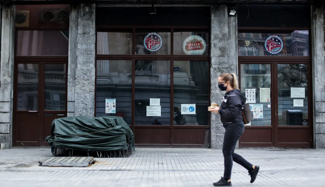 Seseorang berjalan melewati bar yang tutup pada hari kembali diperketatnya pembatasan sosial di Brussel, Belgia, Kamis (8/10/2020). Brussels pada Rabu (7/10), memutuskan menutup semua bar, ruang dansa, dan kafetaria selama sebulan sebagai upaya membendung lonjakan COVID-19. (Kenzo TRIBOUILLARD/AFP)