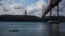 Dua pria berlatih mendayung melewati 25th April Bridge yang terdapat grafiti lumba-lumba di sungai Tagus di Lisbon, Portugal pada 7 Agustus 2021. Lalu lintas laut yang berkurang akibat pandemi corona membuat ekosistem di Sungai Tagus kembali ramah untuk lumba-lumba. (PATRICIA DE MELO MOREIRA / AFP)