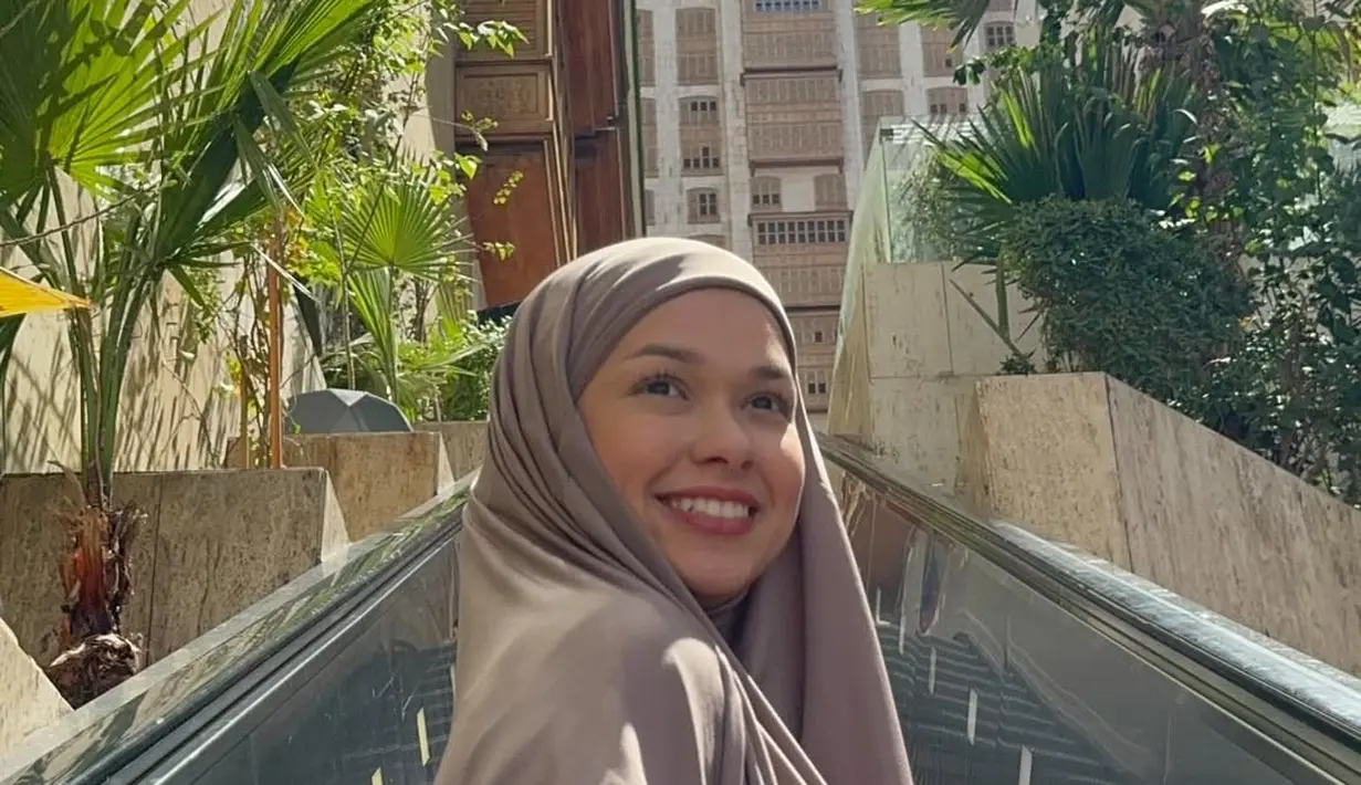 Pada foto lain, ia terlihat mengenakan busana taupe dengan latar arsitektur kota. Warna netral ini memberi kesan modern dan dewasa namun tetap lembut. Senyum lebarnya membuat penampilan terasa lebih hidup dan natural, menunjukkan momen bahagia selama perjalanan ibadah.  [@rklopper].