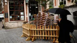 Seorang perempuan berjalan melewati tumpukan kursi dan meja dari bar yang tutup di Brussel, Belgia, Kamis (8/10/2020). Brussels pada Rabu, 7 Oktober 2020, memutuskan menutup semua bar, ruang dansa, dan kafetaria selama sebulan sebagai upaya membendung lonjakan COVID-19. (AP Photo/Francisco Seco)