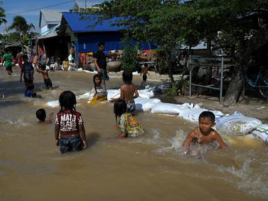 Anak-anak bermain di air banjir setelah hujan lebat di pinggiran Phnom Penh, Kamboja (26/10/2021). Kementerian Sumber Daya Air dan Meteorologi telah mengeluarkan pemberitahuan pada hari Senin tentang situasi cuaca, mengkonfirmasikan risiko banjir di 14 ibu kota dan provinsi Kamboja. (AFP Photo)