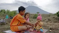 Anak-anak duduk di areal perkebunan dengan latar belakang Gunung Agung di Karangasem, Bali, Rabu (29/11). Meskipun Gunung Agung terus menunjukkan peningkatan aktivitas vulkanik, sebagian warga memilih tetap beraktivitas. (AP/Firdia Lisnawati)