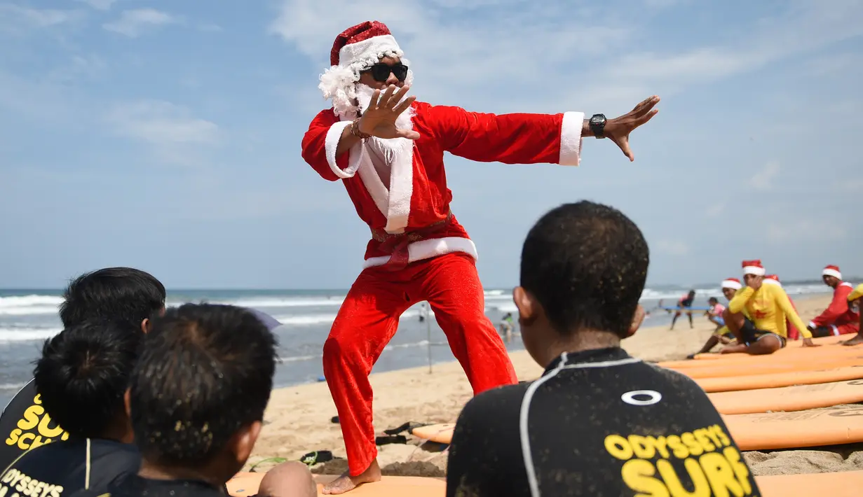 Seorang pria berkostum Santa Claus memberikan pelatihan selancar kepada sejumlah anak di Pantai Kuta, Bali, Senin (10/12). Setiap tahunnya, ribuan wisatawan mendatangi Bali saat menjelang natal dan tahun baru. (AFP PHOTO / Sonny Tumbelaka)